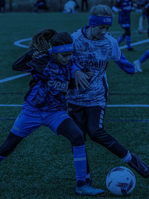 Two soccer players in blue uniforms competing for the ball on a green field.