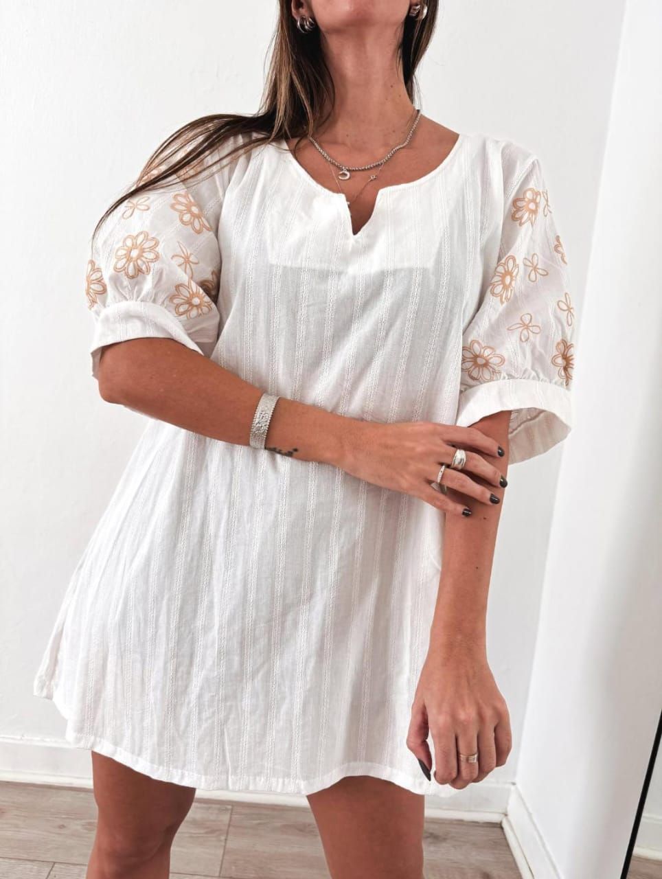Mujer con vestido blanco con mangas florales, posando en el interior.
