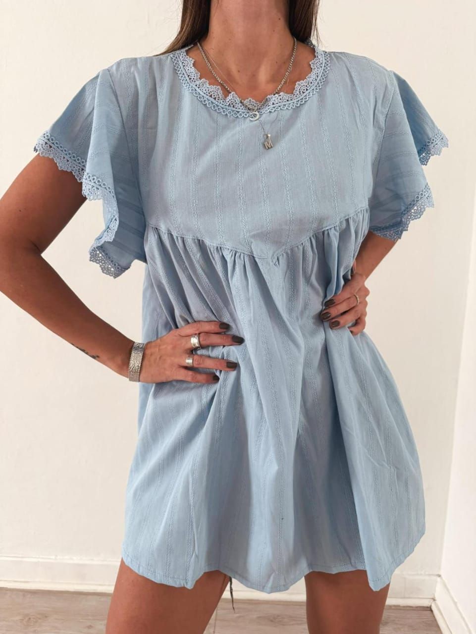 Mujer con vestido de rayas azules con ribete de encaje, manos en las caderas.