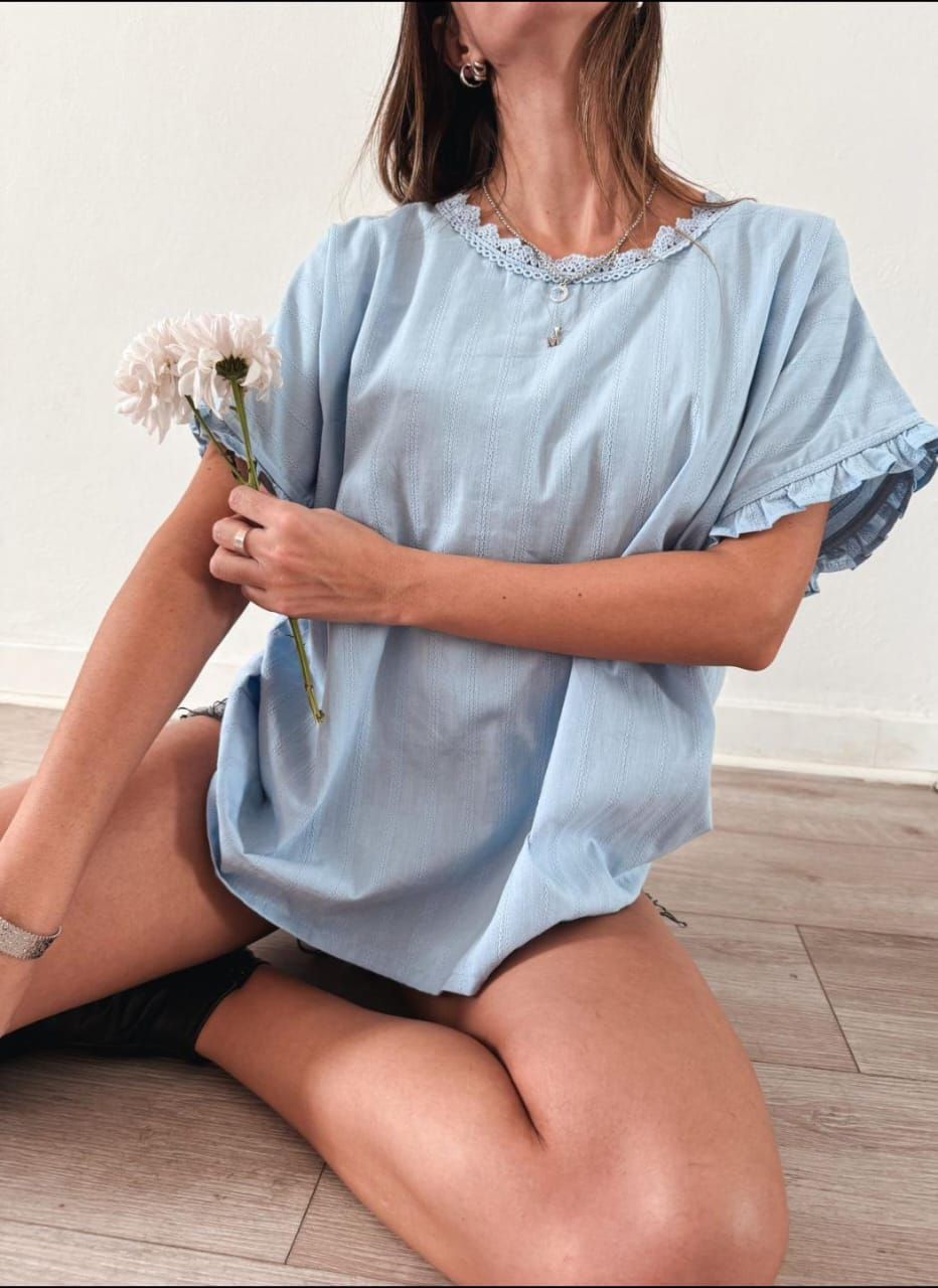 Mujer con top azul sostiene una flor, sentada en el suelo.