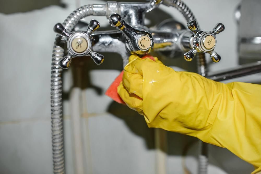 A Person Wearing Yellow Gloves Is Cleaning a Faucet — Professional Cleaning Company in Childers, QLD