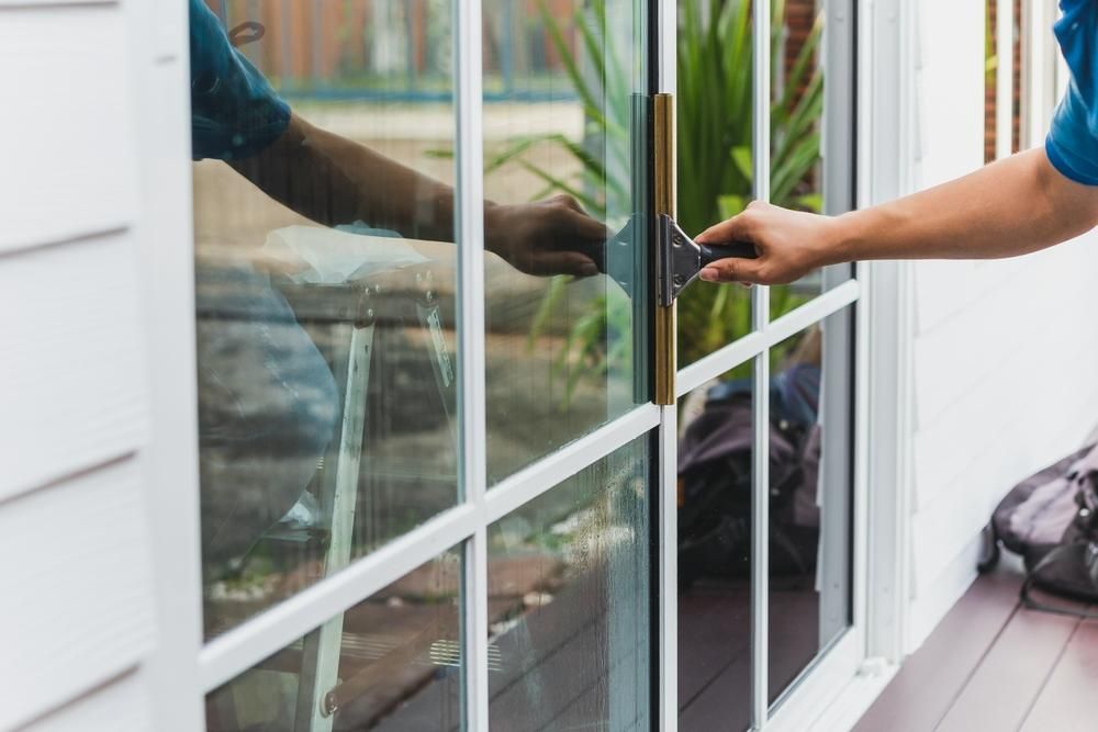 A Man Is Cleaning a Sliding Glass Door — Professional Cleaning Company in Toogoom, QLD