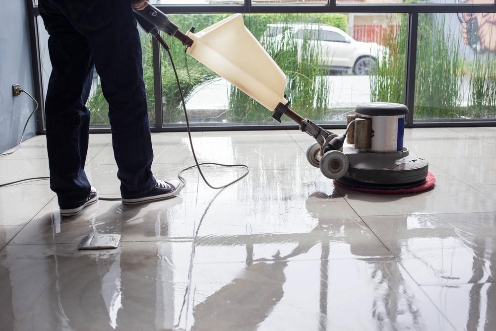 A Man Is Cleaning a Tiled Floor with A Machine — Professional Cleaning Company in Burrum Heads, QLD