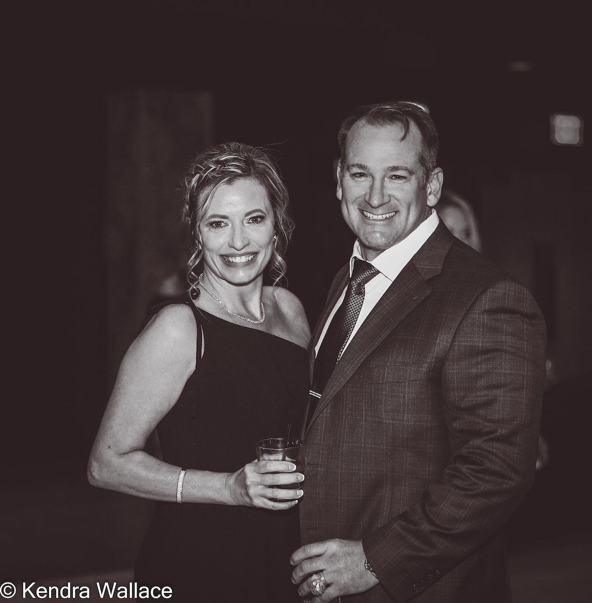 Woman and man in formal wear, smiling. Woman holds a drink. Black and white photo.