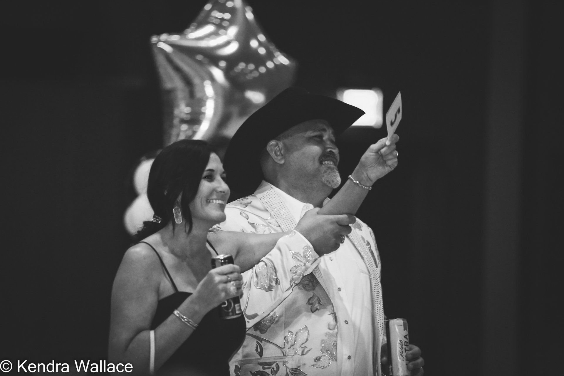 Man in cowboy hat holds up number, woman smiles; party setting.