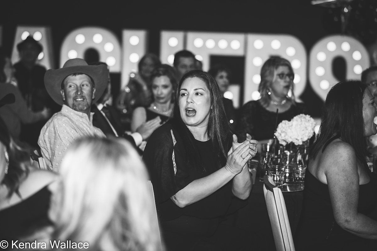 People clapping at an event, lit sign in the background.
