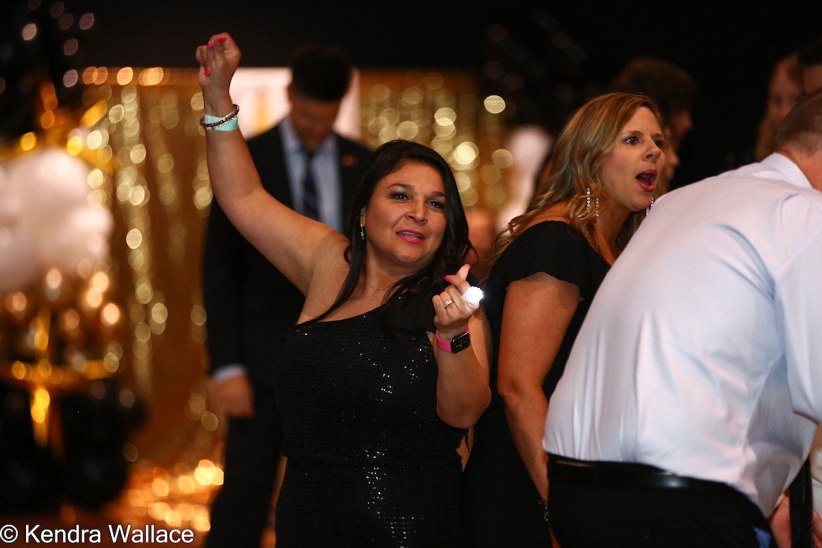 Woman in black dress dancing at a party, arm raised. Gold and black decorations in the background.