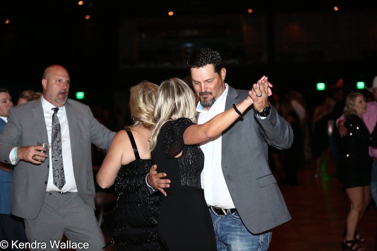 People dancing at a formal event, two couples. Man in grey suit watches.
