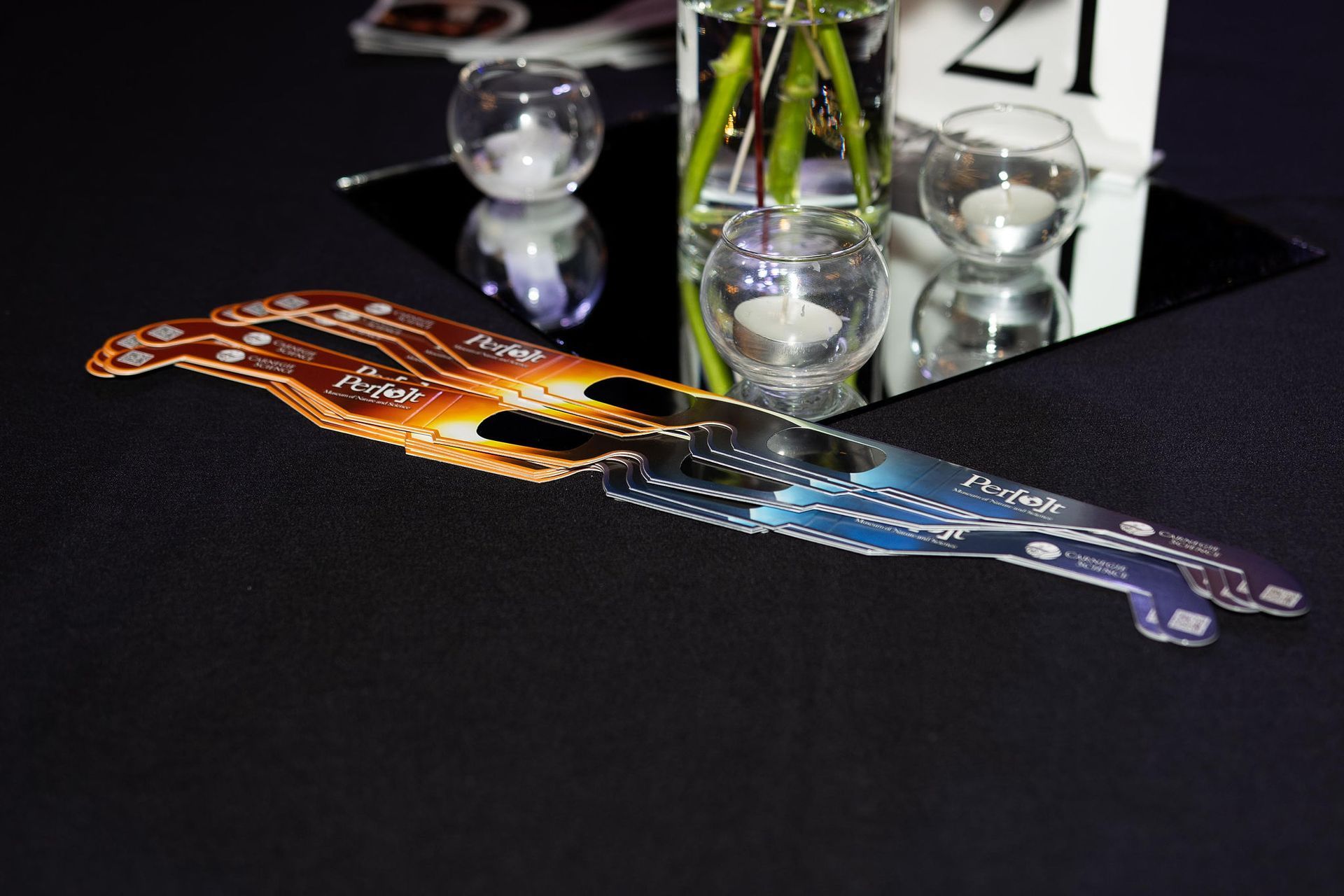 A colorful, stylized object, likely a table decoration, rests on a black tablecloth near a table number and candles.