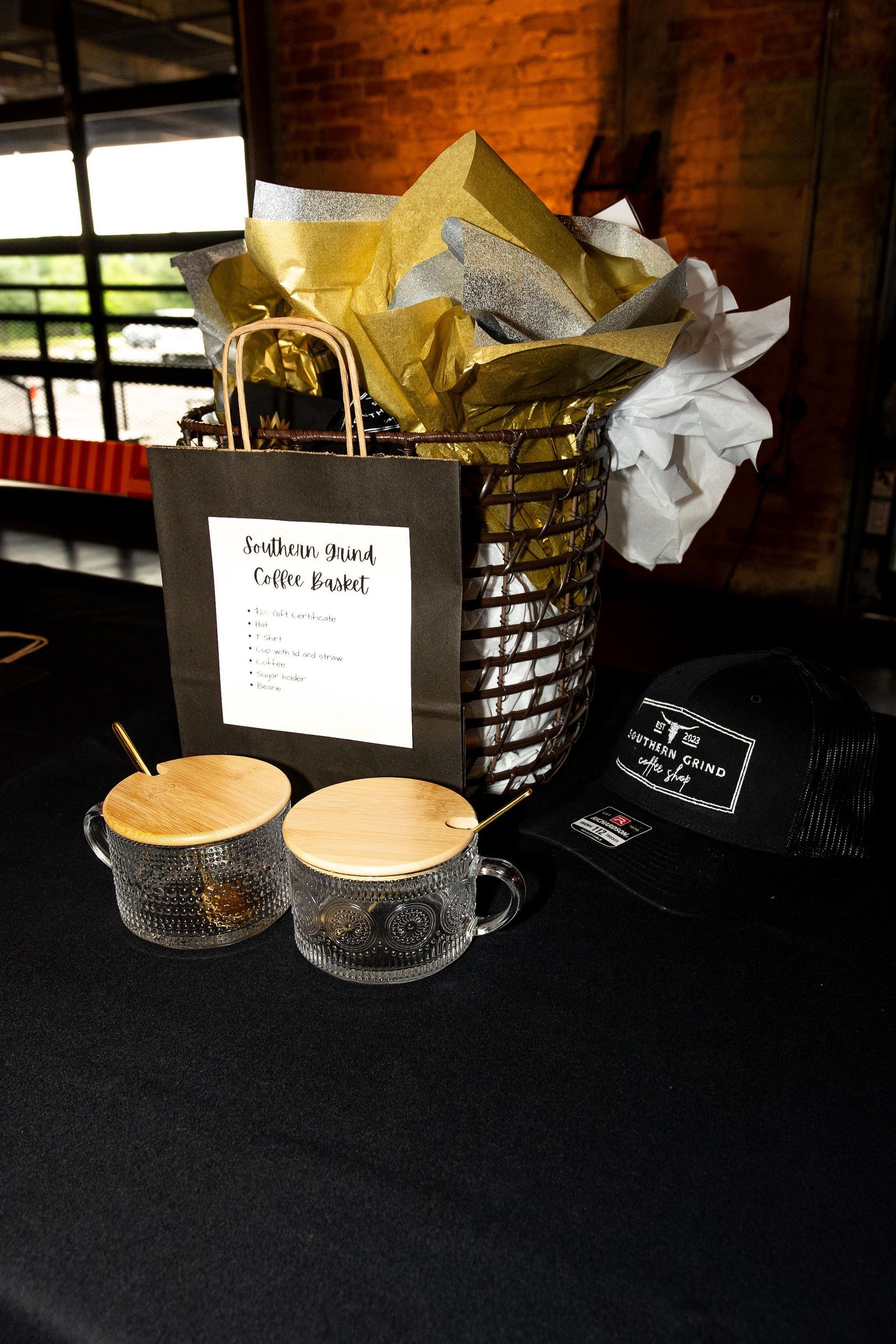 Two coffee drinks, gift bag, and cap on a black table with decorative container.