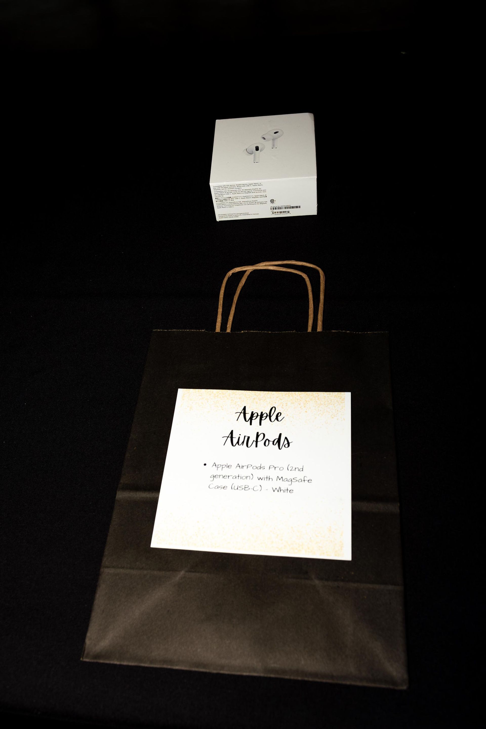 Black shopping bag and white box on black surface. Bag has a label 