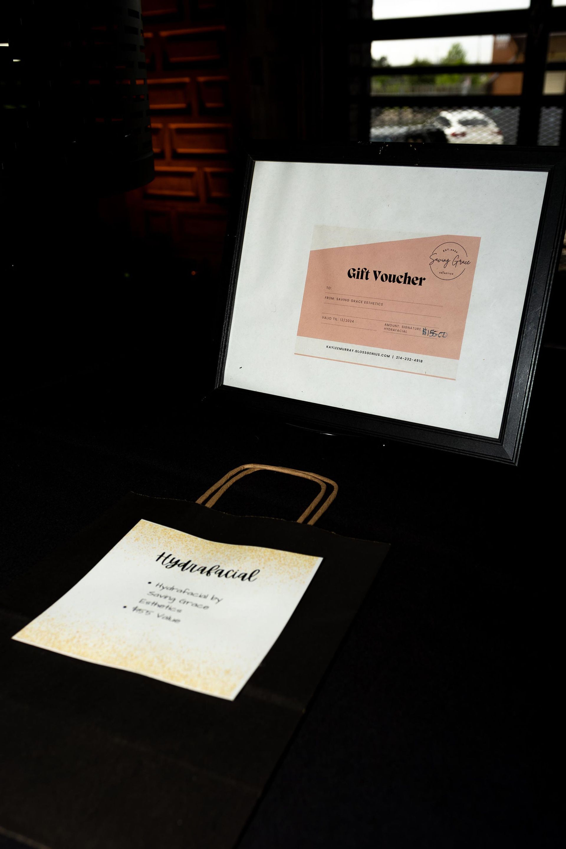 A black table displays a bag with a handwritten note, and a digital screen with a similar document, set indoors.