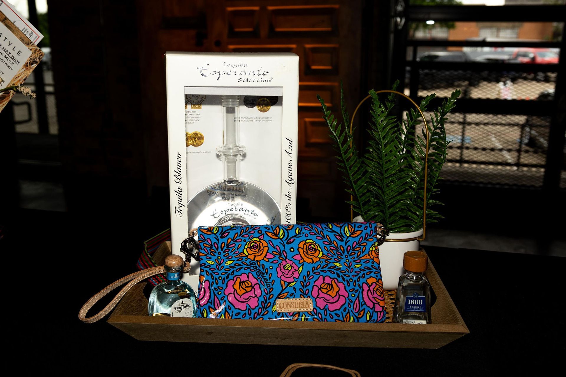 A wooden tray with a glass, patterned clutch, perfume, and plant.