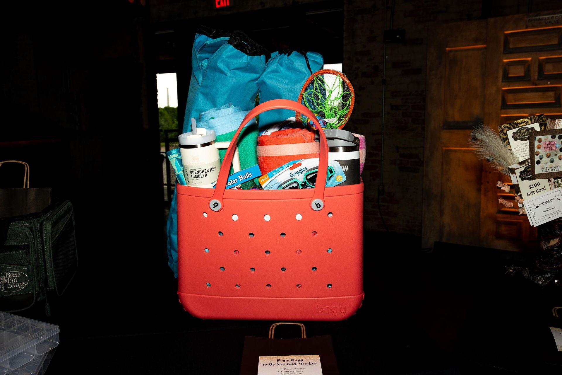 Red tote bag filled with items, including mugs, on a table inside a building.