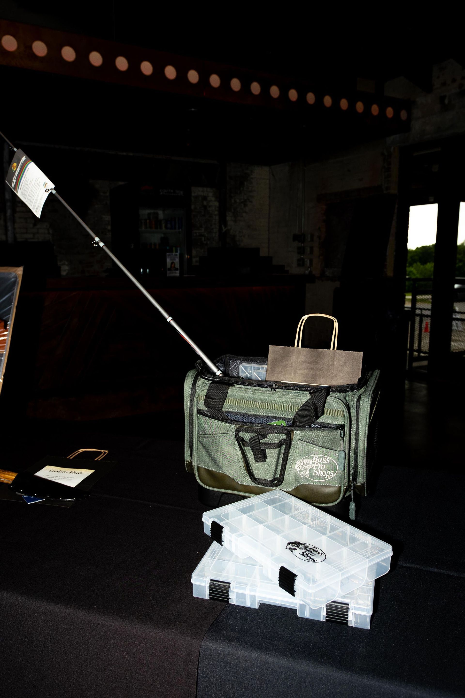 Fishing tackle bag with rod, open tackle boxes on a dark surface.