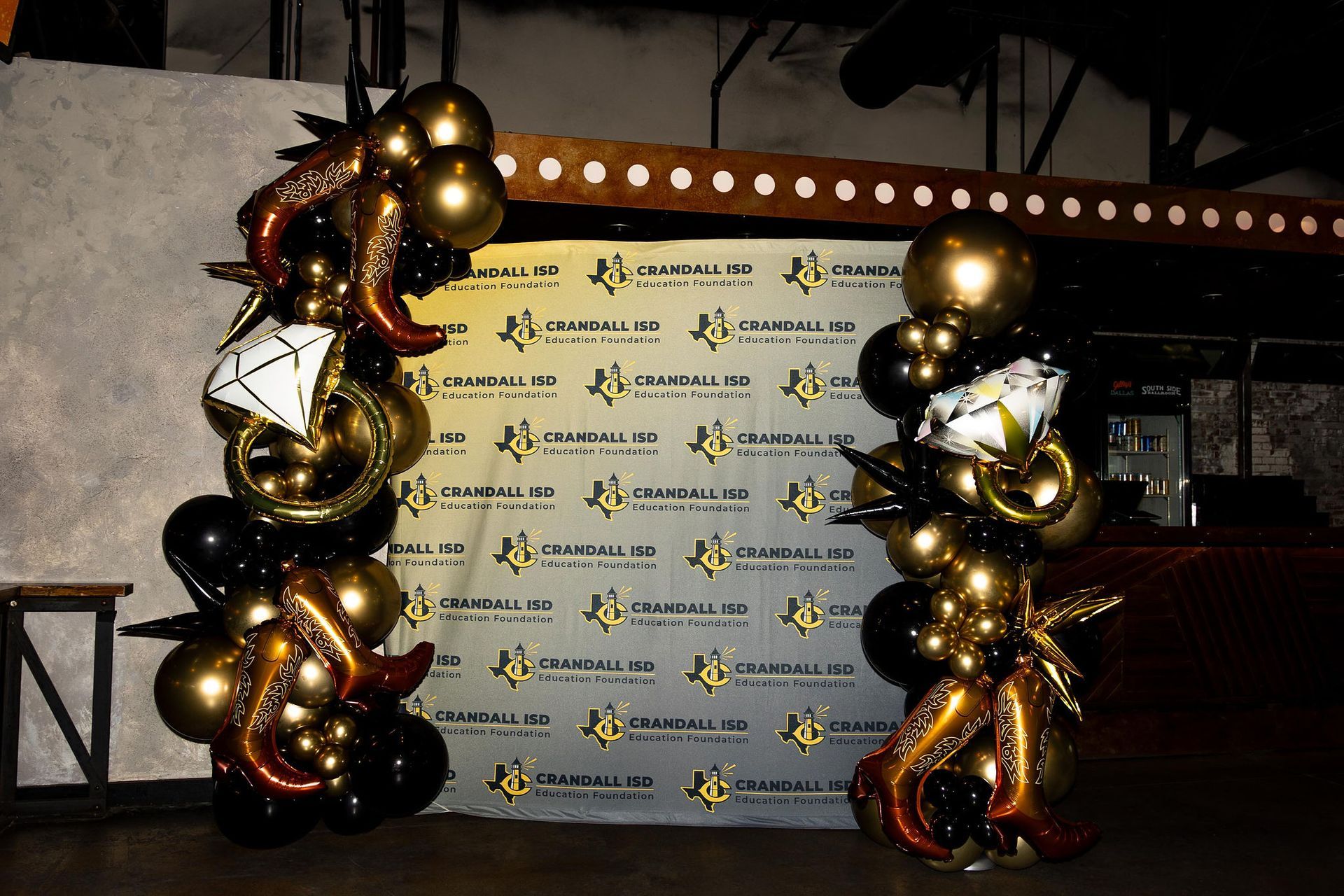 Two balloon columns, black and gold, flank a banner at an event.