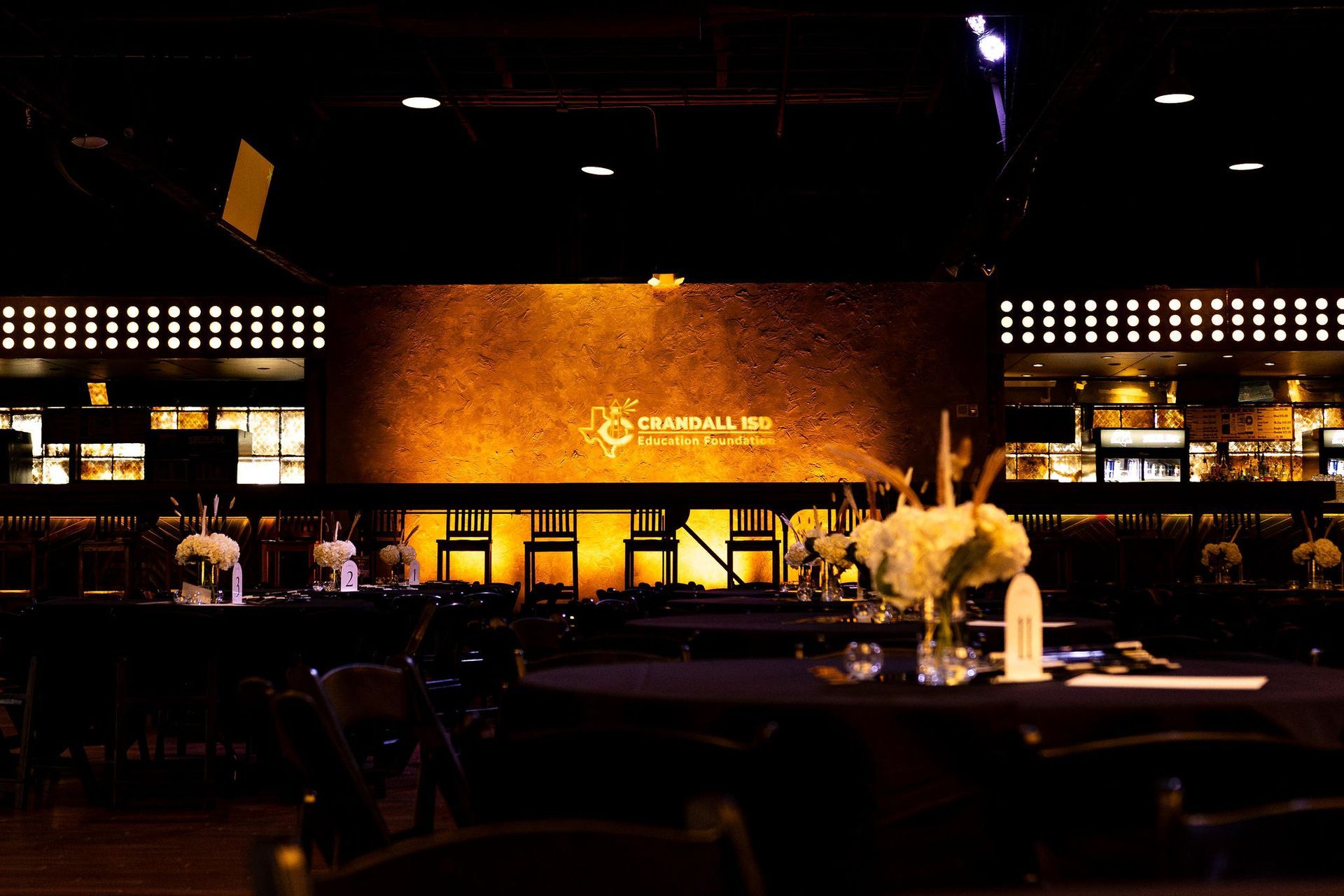 An event space with tables, chairs, and a stage with a gold-lit backdrop.
