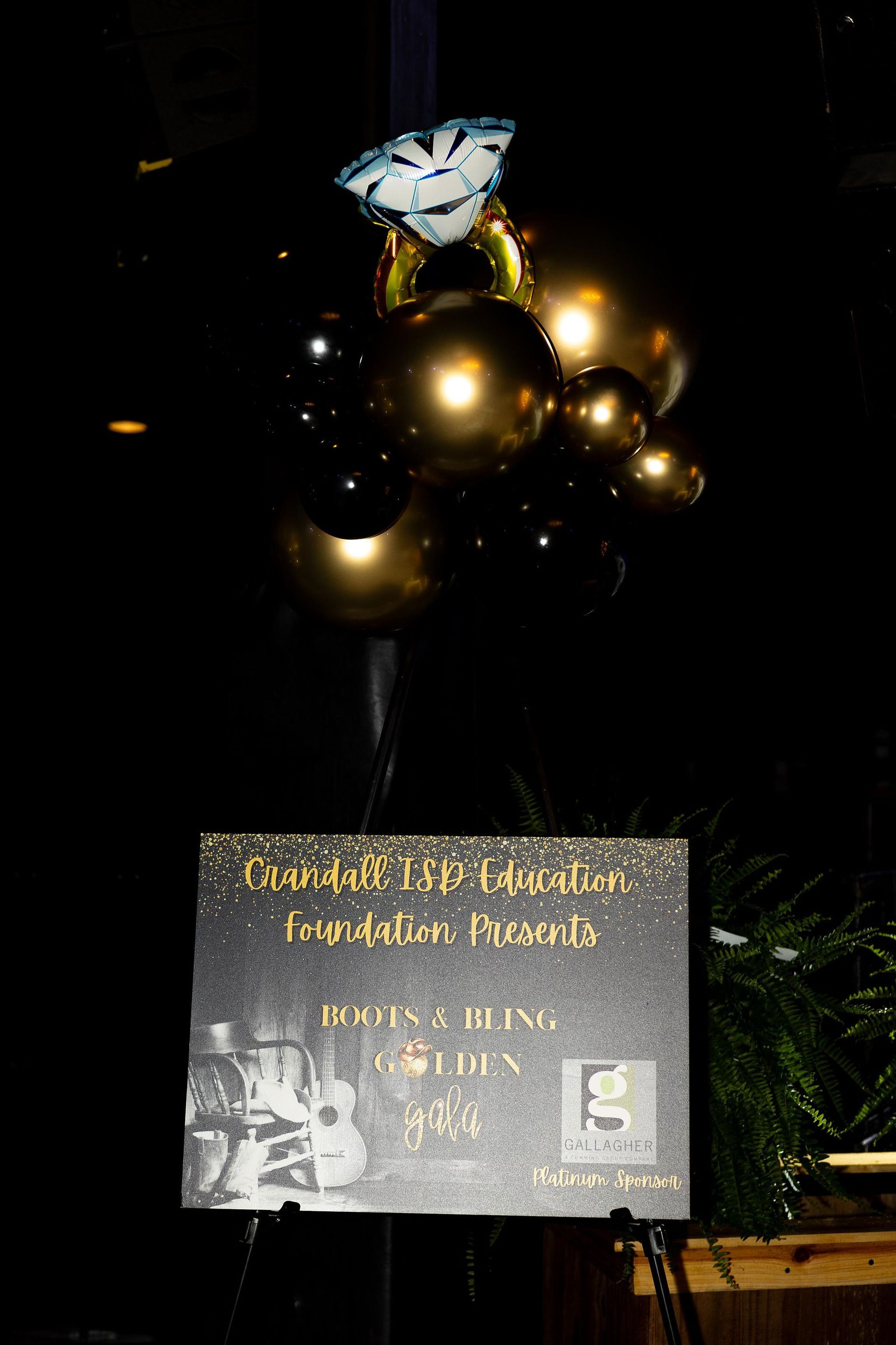 Sign for event with balloons. Gold, black, and blue decor.