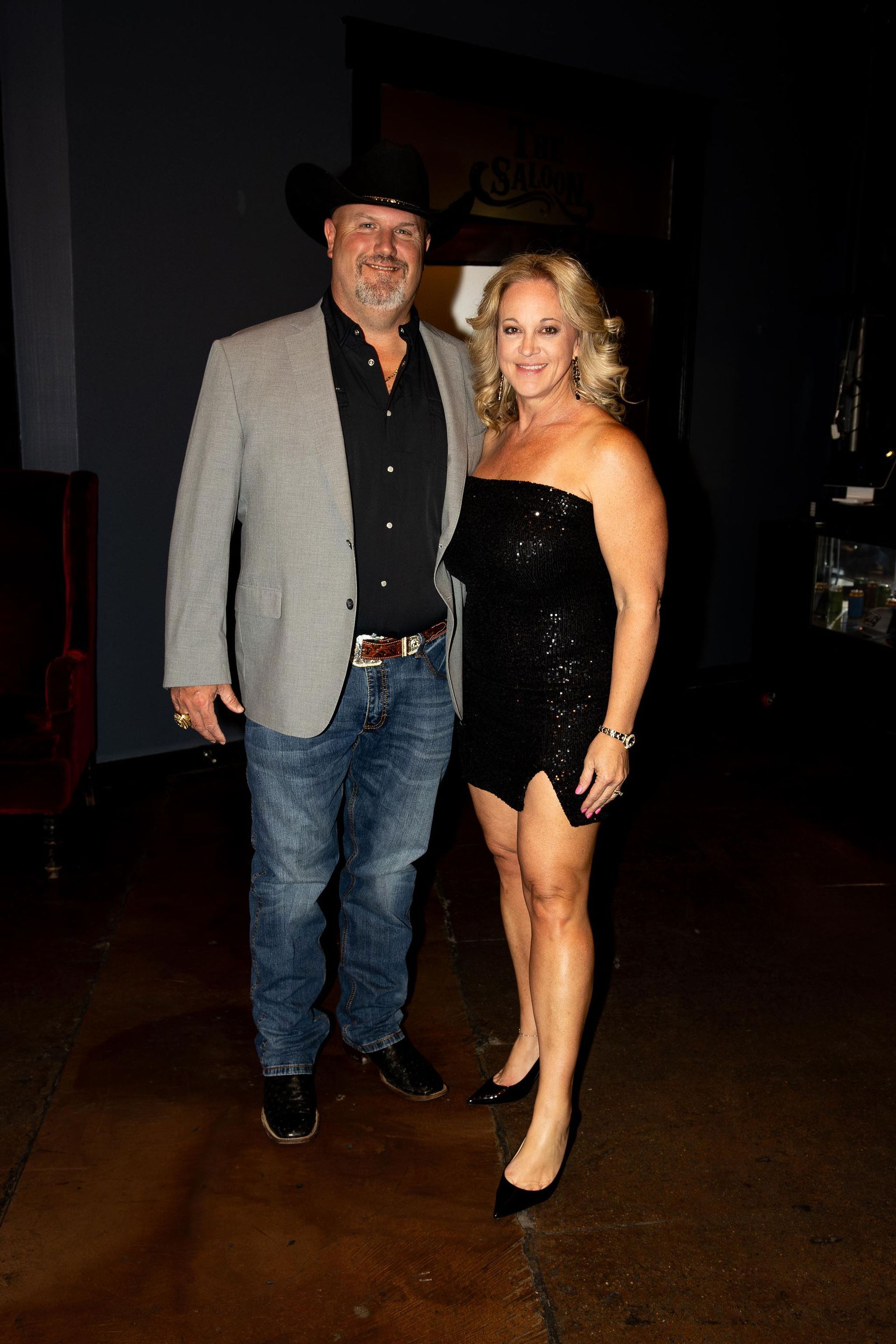 Man in cowboy hat and woman in a sequin dress pose together in a dim setting.
