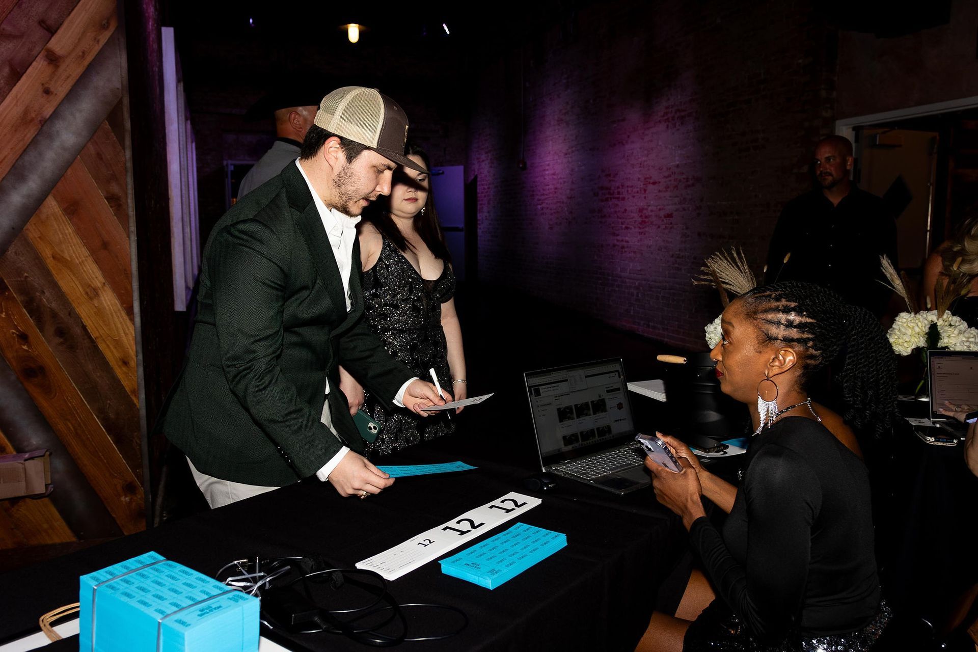 People at a registration table. Man in jacket signs, woman checks a list.