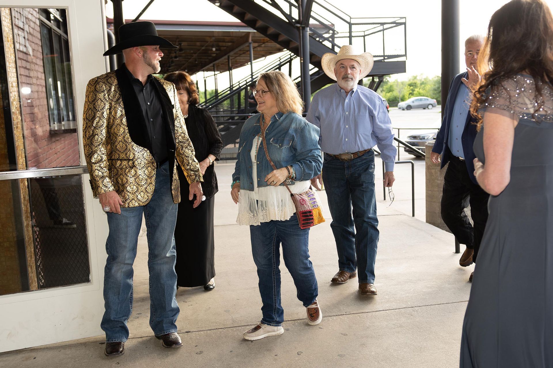 People in Western attire entering a building. A man in a gold jacket and hat. Others wear jeans, denim, and cowboy hats.