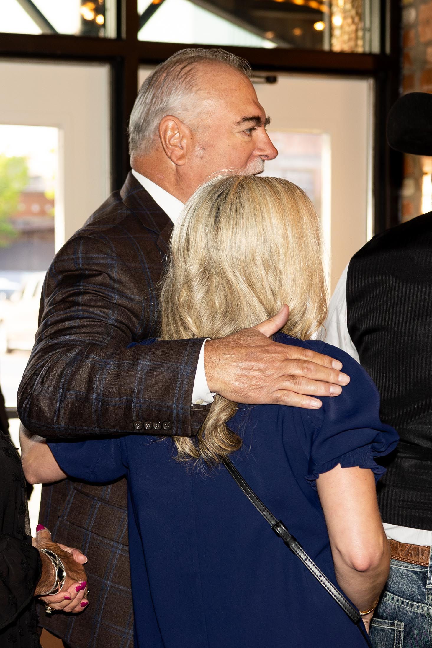 Man in brown blazer hugs woman in blue dress.