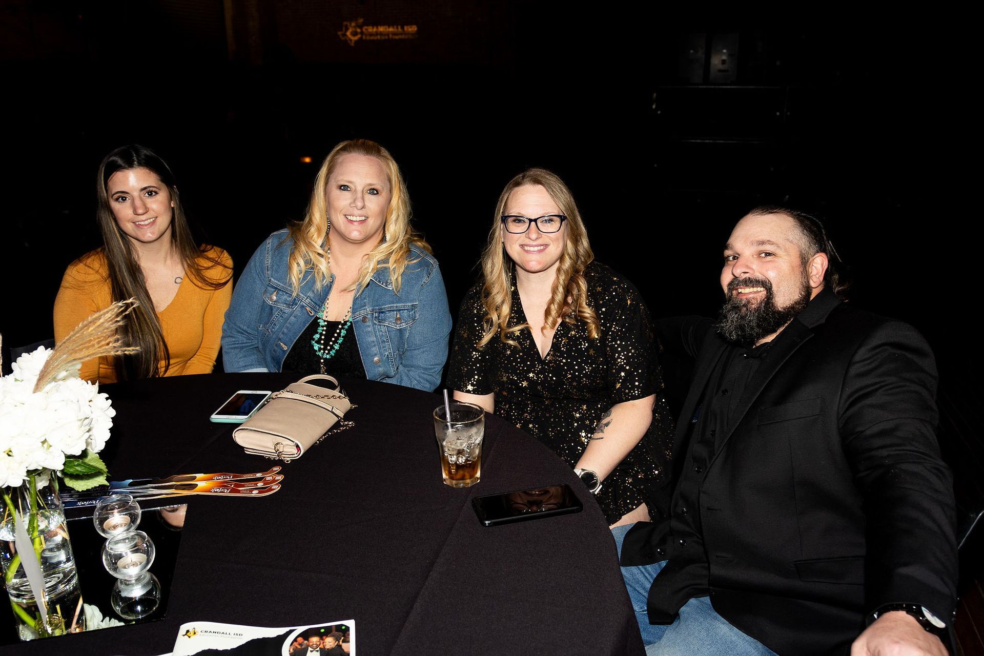 Four people, two women and two men, sit at a table, dark setting.