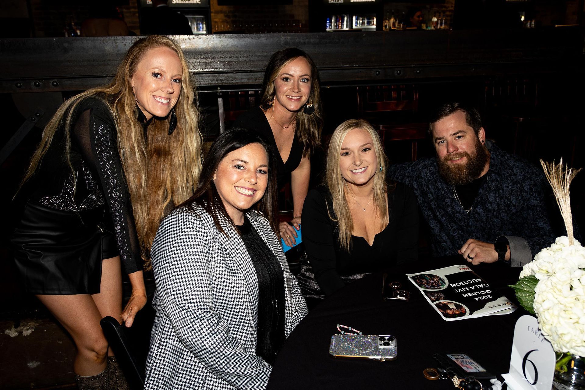 Group of people, mostly women, at a table with food and decor, smiling and looking at the camera.