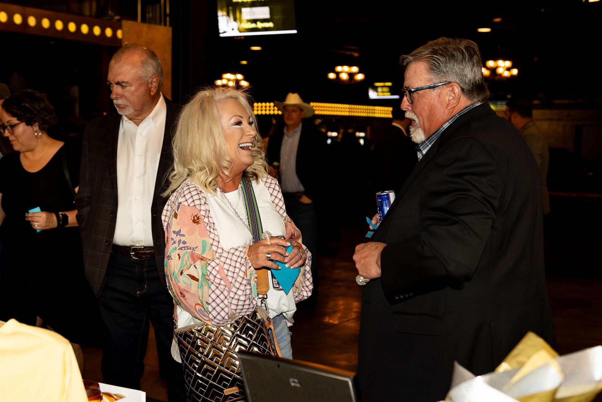 People at an event, woman in bright top laughs while talking to a man. Other people in background.