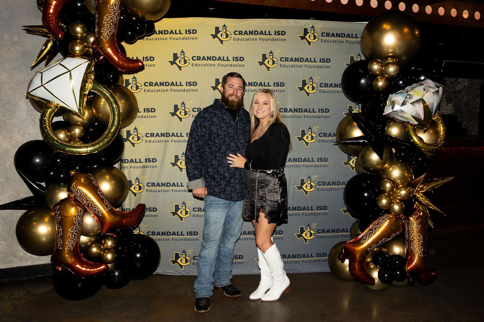 Couple posing in front of a Crandall ISD event backdrop with balloon decorations.