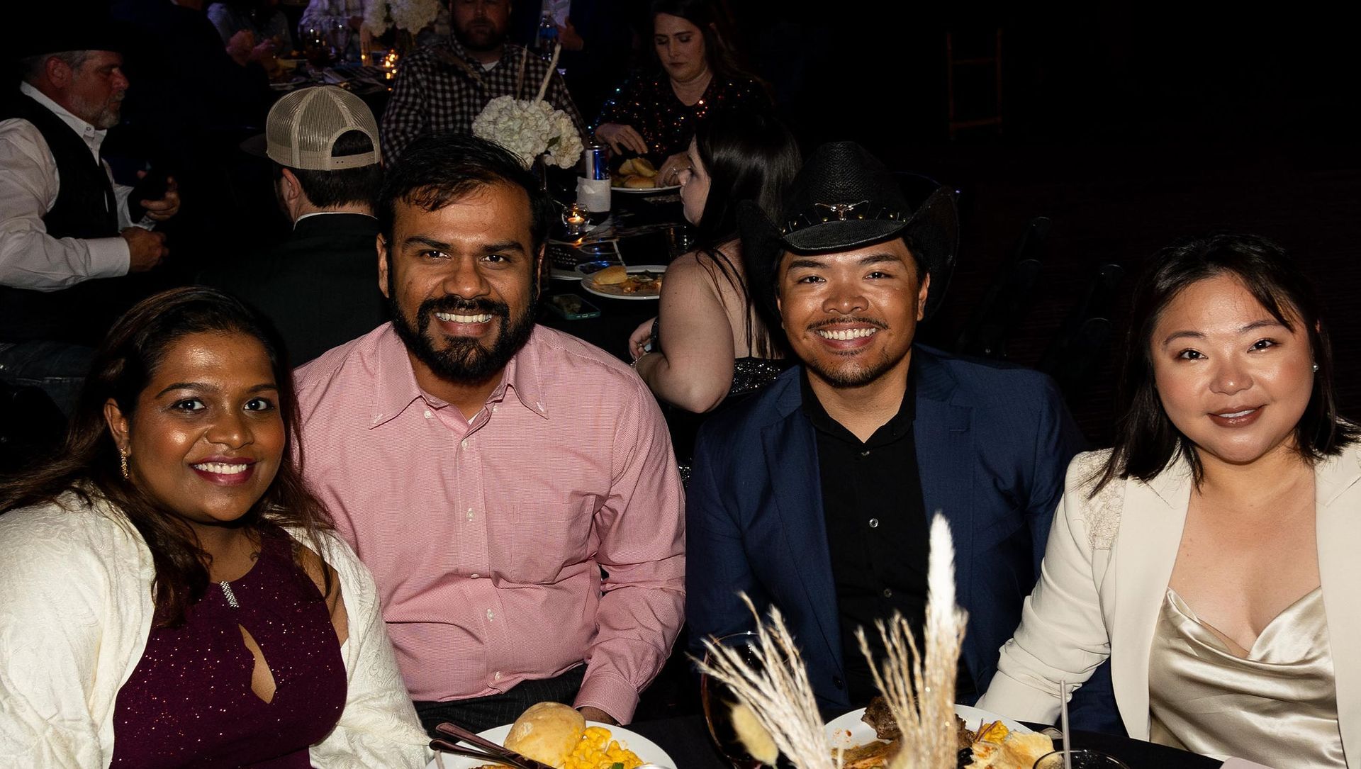 Four people smiling at a table. Two women, two men. Festive setting with dark background.