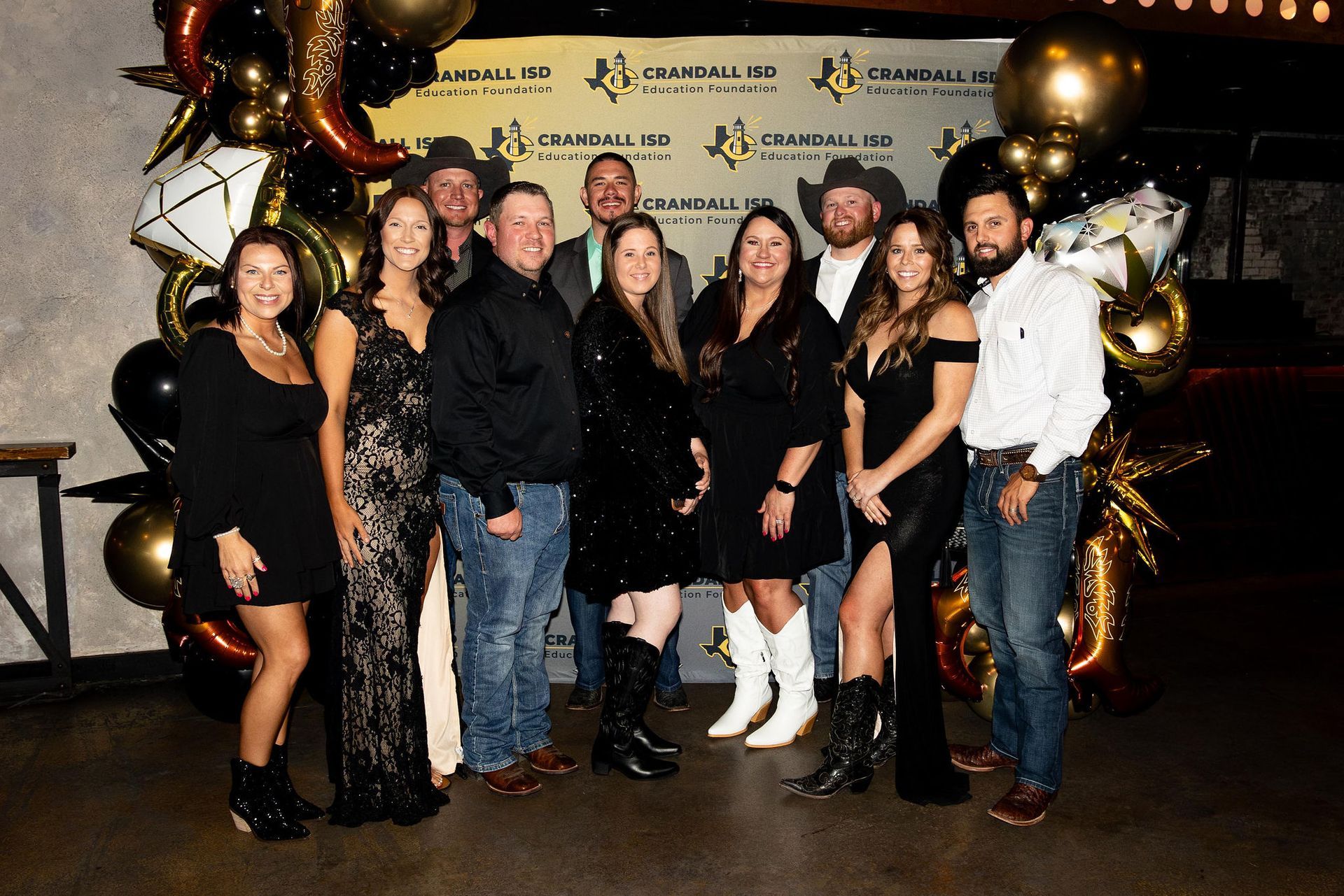 Group of people at an event posing for a photo, black and gold color scheme, some wearing cowboy hats.