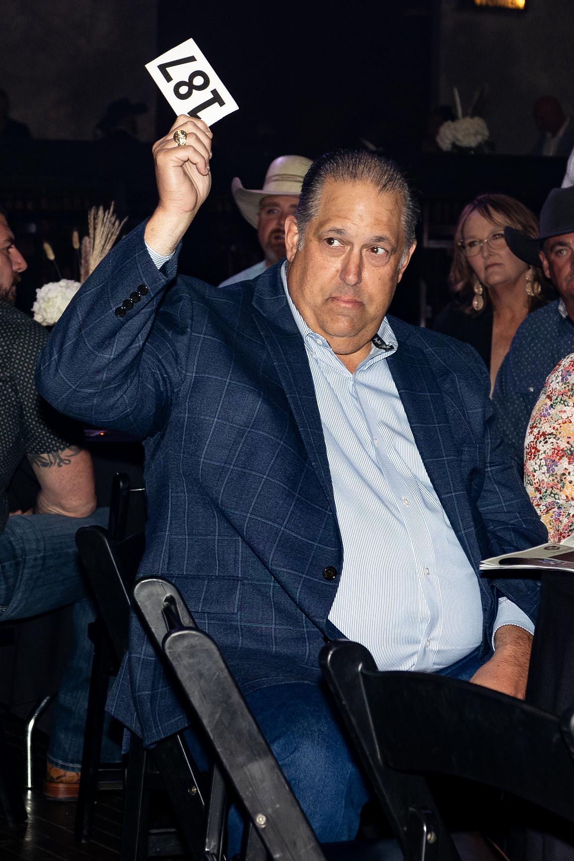 Man in blue blazer at an auction, holding bid paddle 187.
