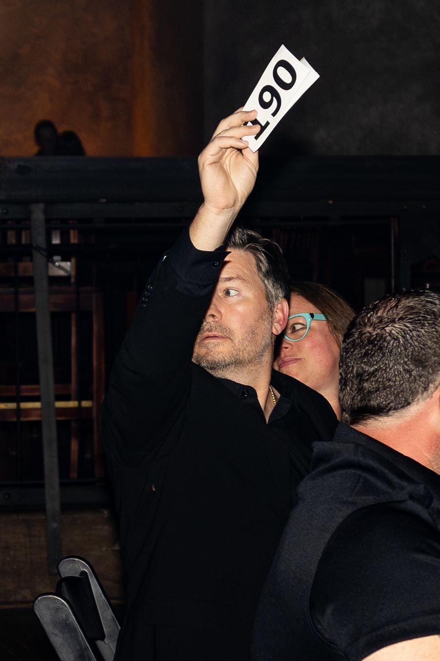 Man in black raises a paddle (number 061) at an auction; indoor setting.