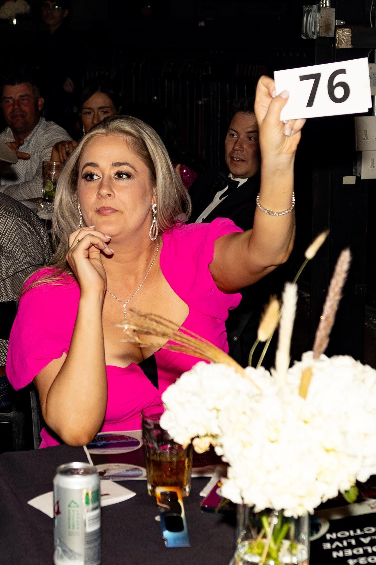 Woman in a pink dress raises a bid number at an auction.