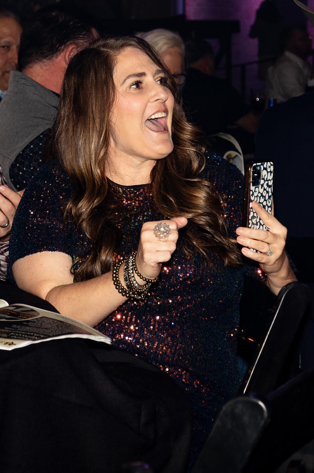 Woman in a sequined dress, taking a selfie, laughing with excitement, indoors.