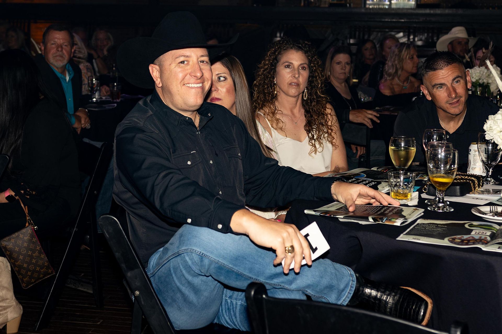 Man in cowboy hat smiles at table; event setting.