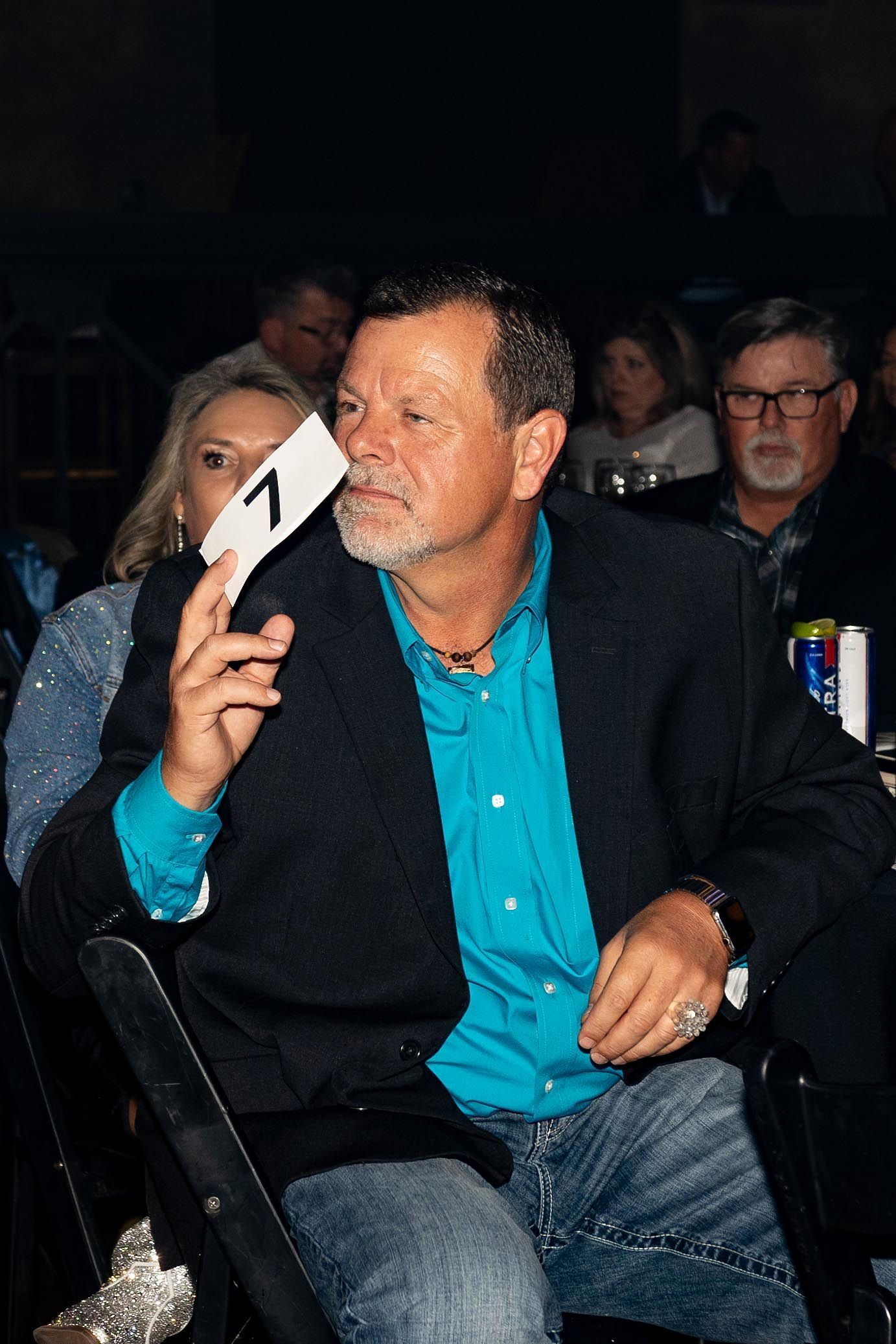 Man in blue shirt and blazer holding bid card 