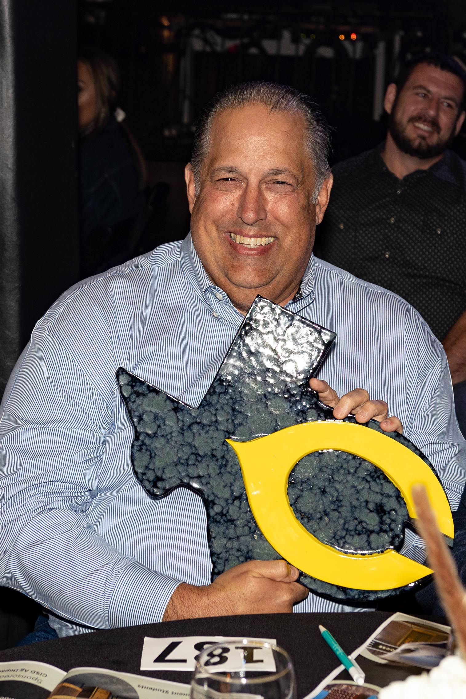 Man smiling, holding an award with a black and yellow 