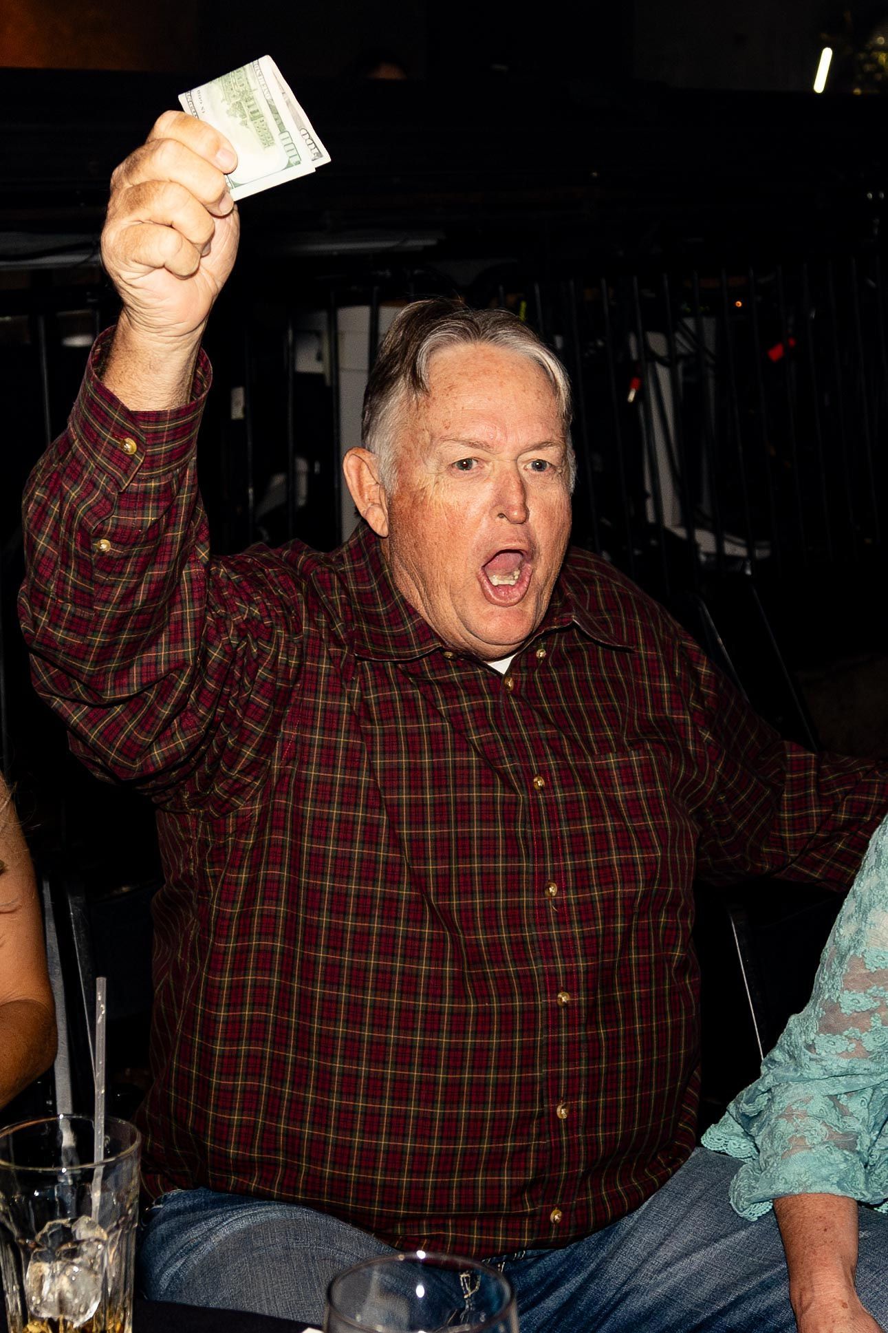Man in plaid shirt holding up money, yelling. Nighttime, outdoors.