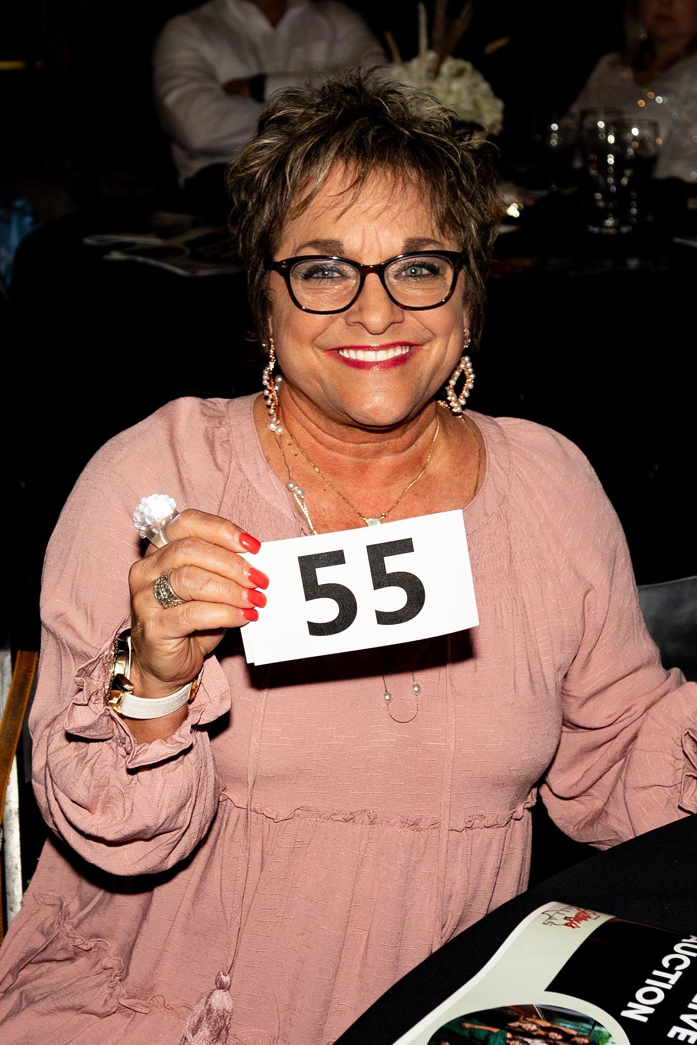 Woman with glasses holding a bid number 