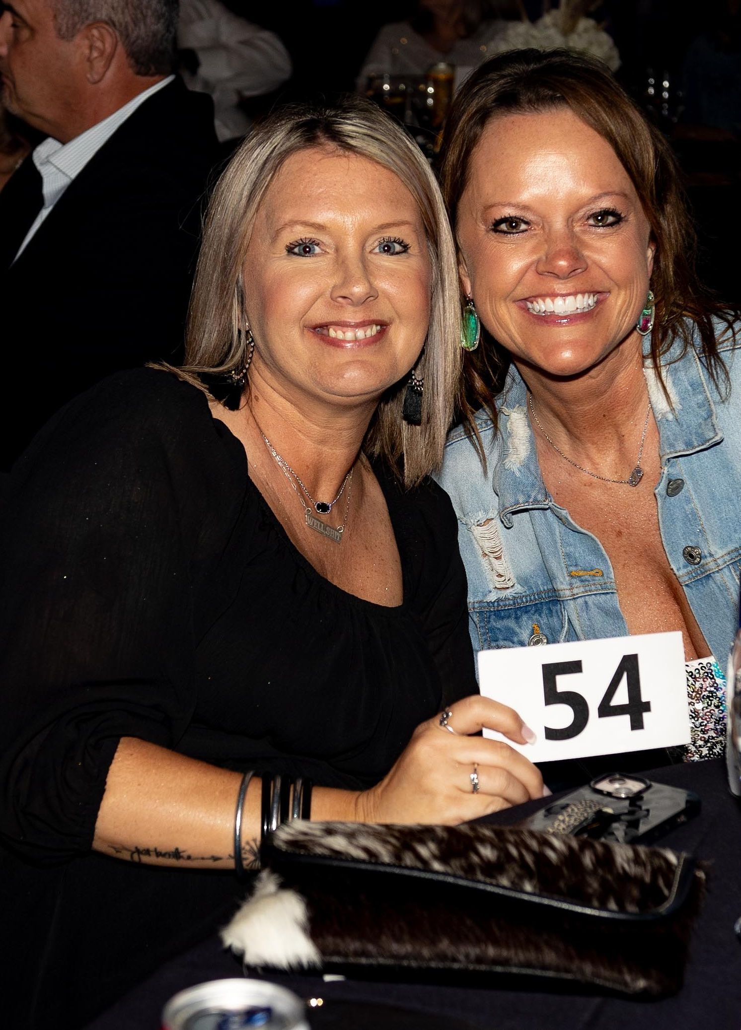 Two smiling women at a table; one holds a 