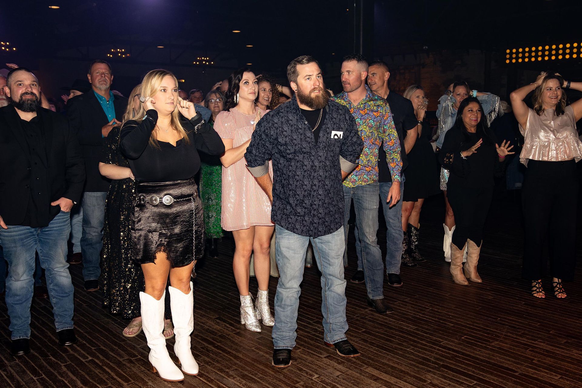A group of people on a dance floor; some are dancing, dressed in casual clothing; indoor, evening.
