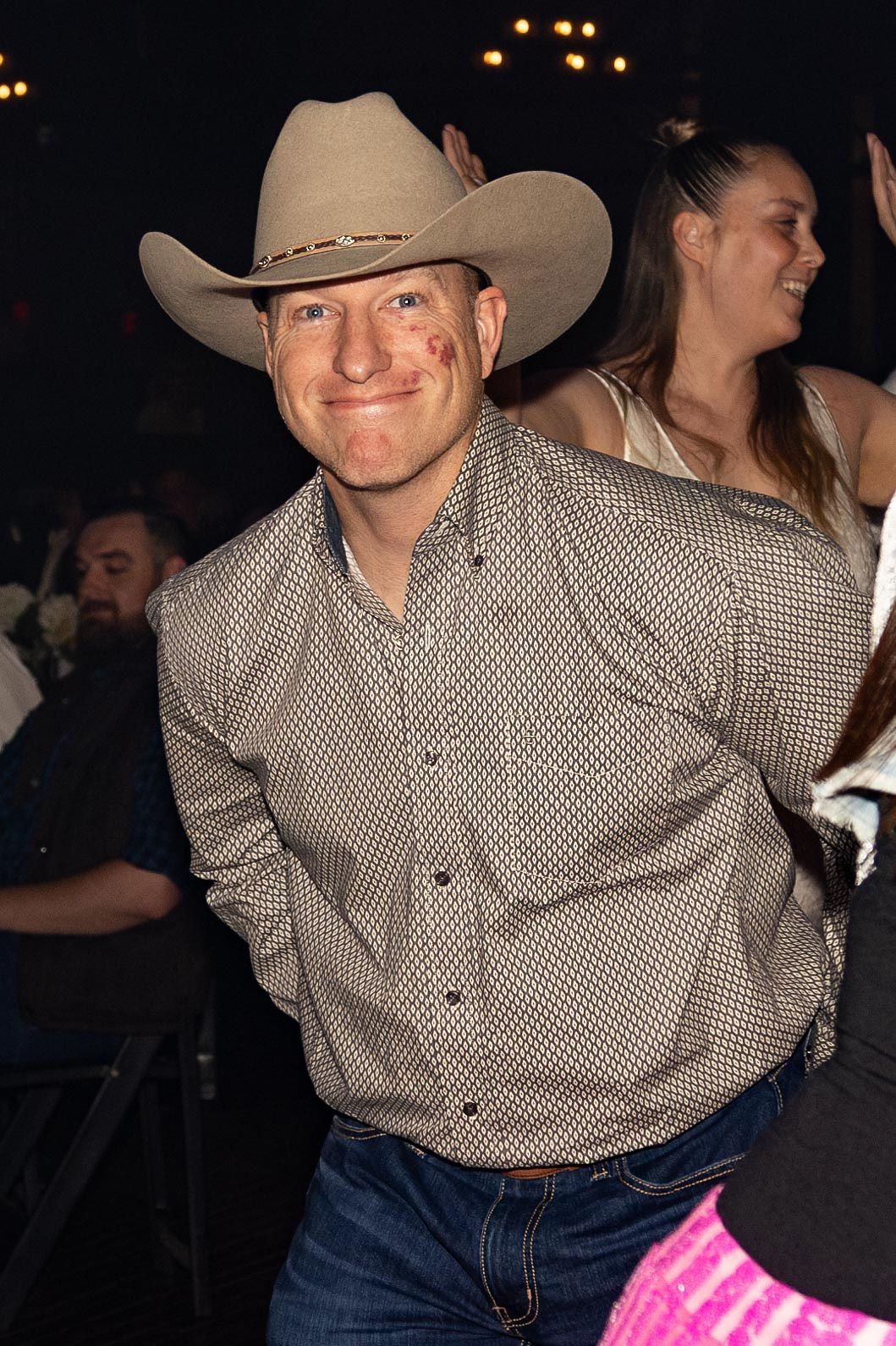 Man in cowboy hat and shirt smiles in a crowded room.