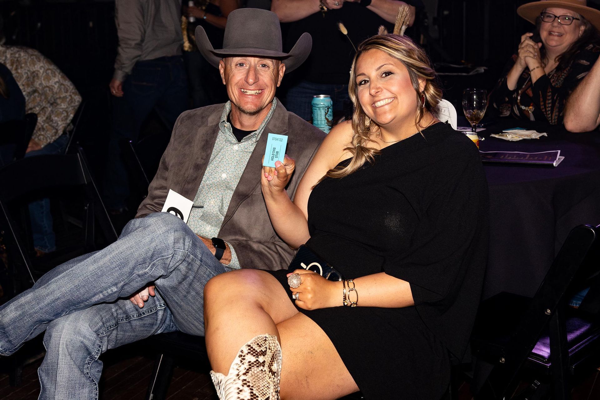 Man in cowboy hat and woman smile, holding a ticket at an event.