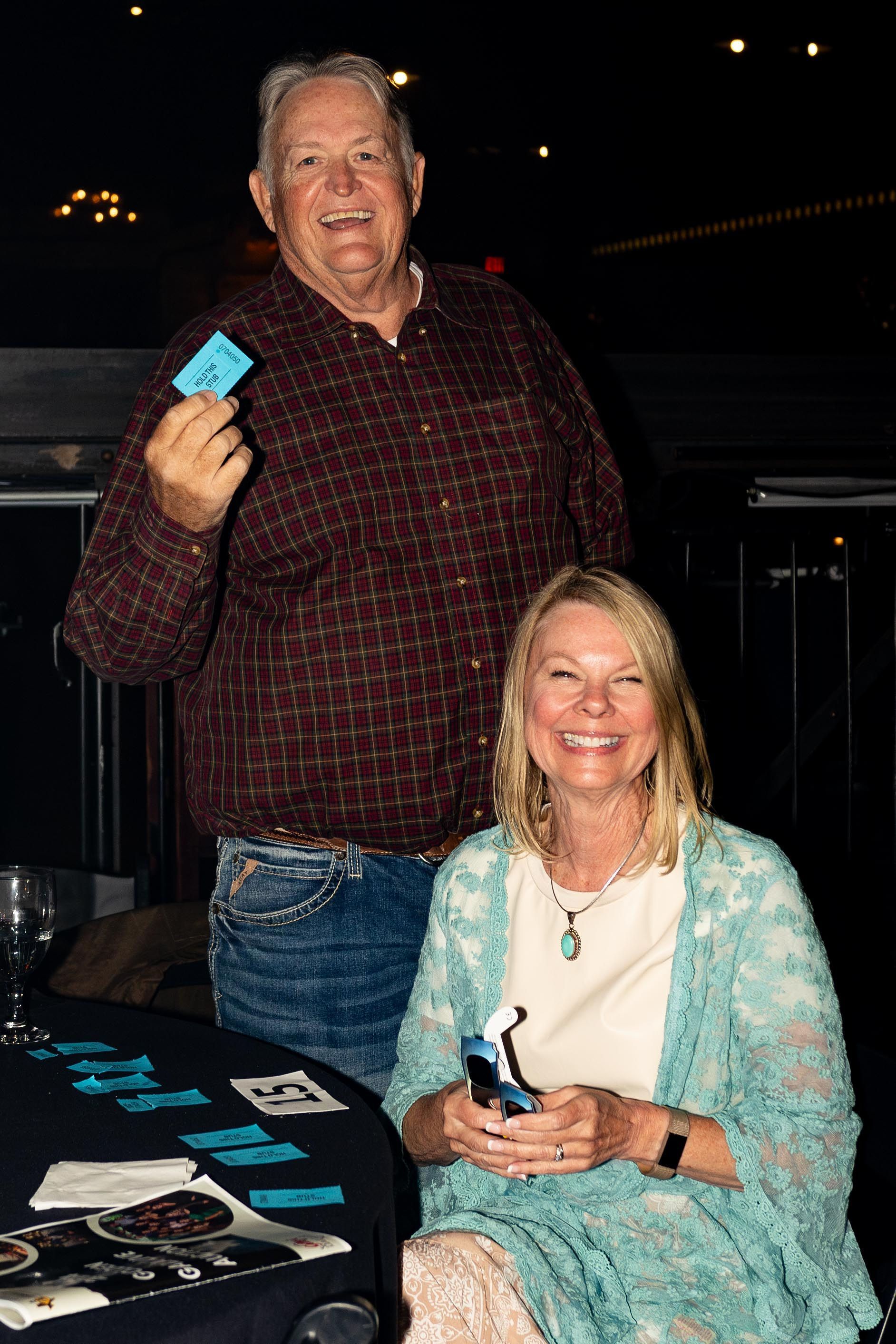 Man holds ticket, smiling next to a woman, at an event.