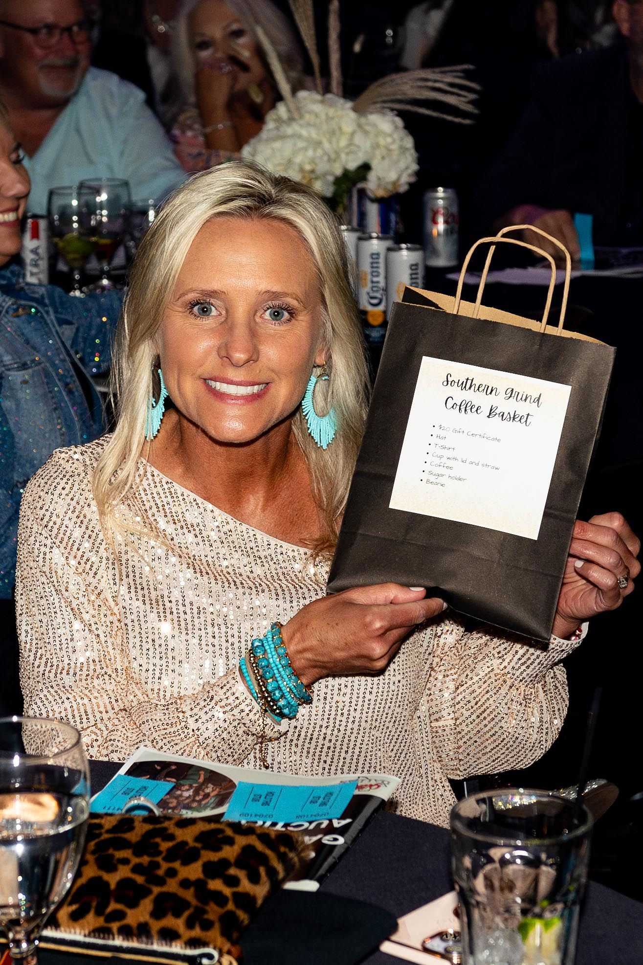 Woman holding a gift bag, smiling at a gala, wearing turquoise jewelry and a patterned top.