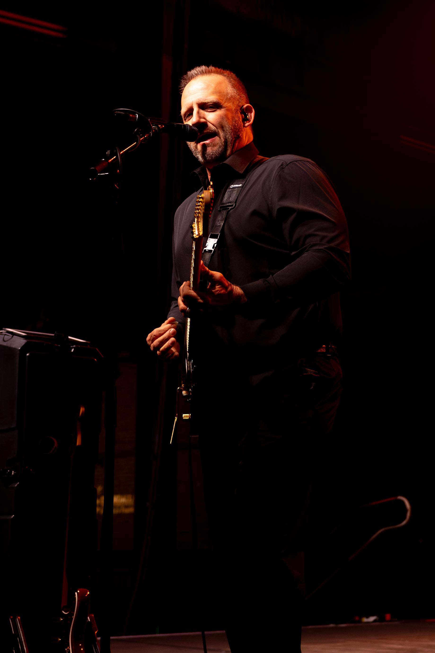 Man with a guitar singing and playing on stage, dark lighting.