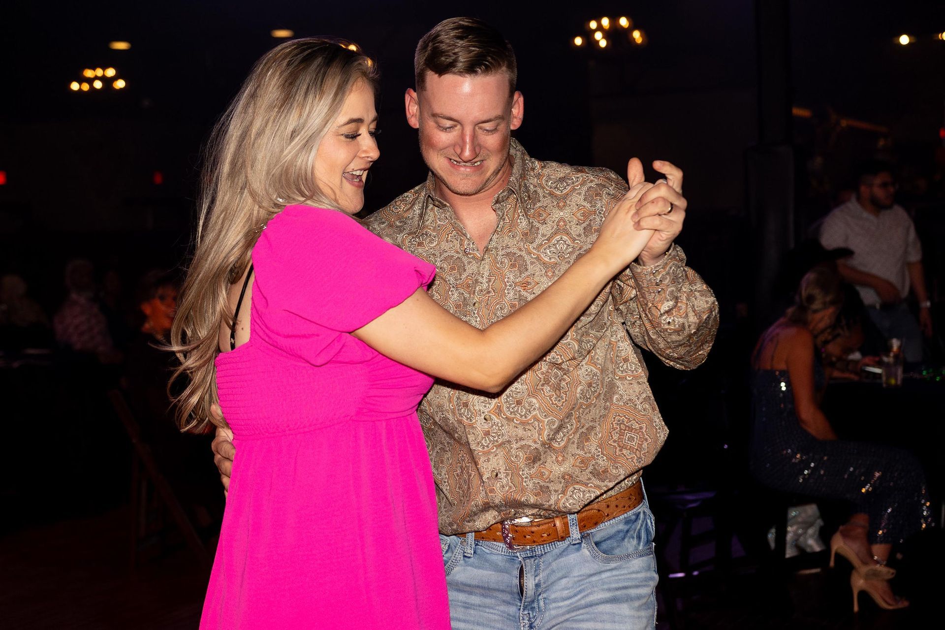 Woman in pink dress and man in paisley shirt dancing. Interior, smiling.