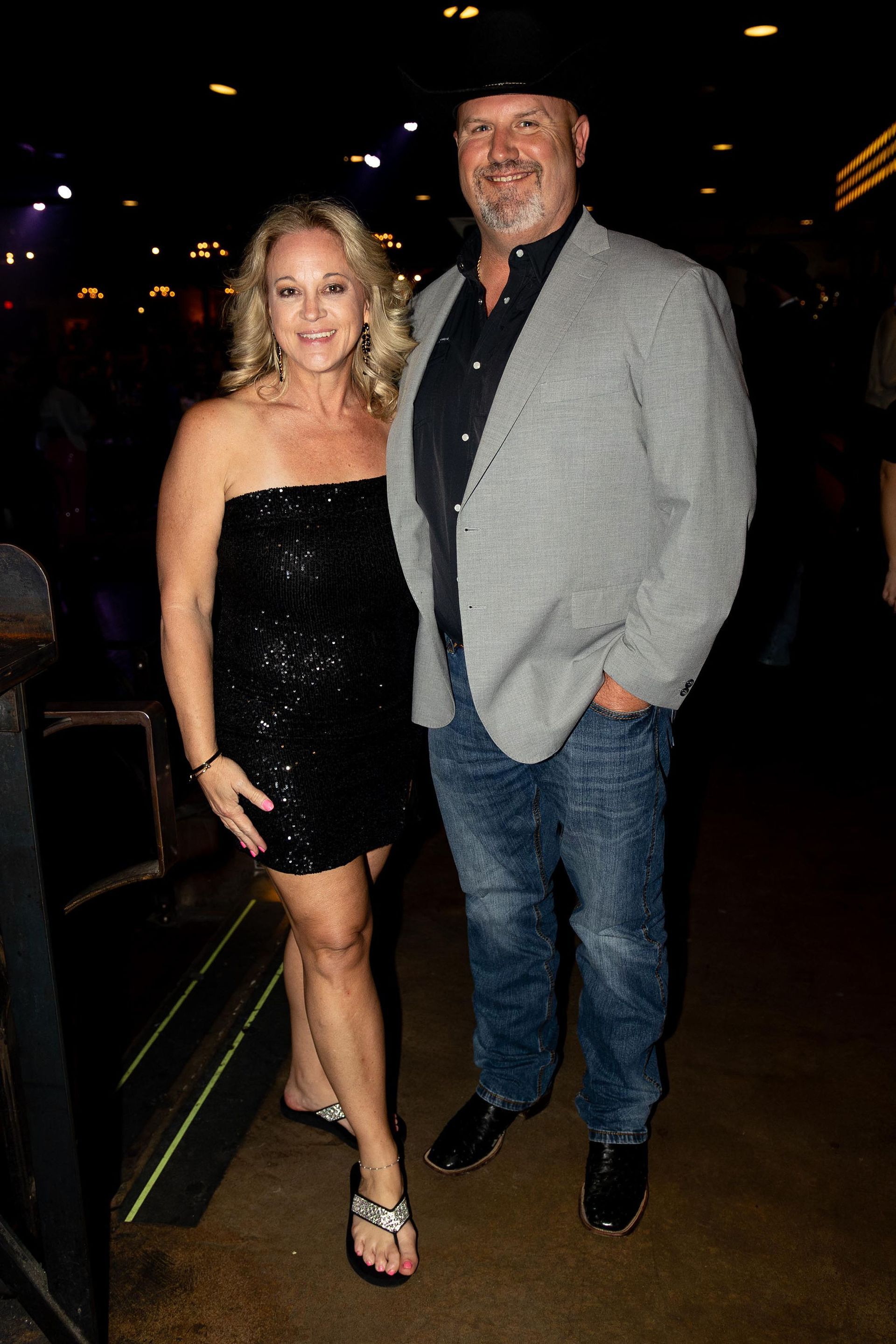 Woman in black sequin dress and man in cowboy hat, posing for photo indoors.